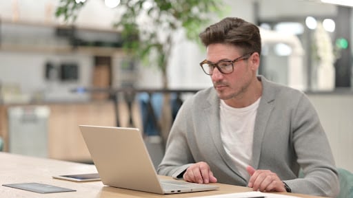 A man wearing eyeglasses working intently in front of his laptop.