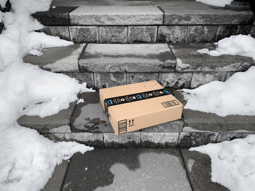 An Amazon parcel found on a cement stairway surrounded by snow.