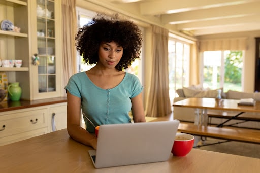 A Latina woman working in front of her laptop in her kitchen.